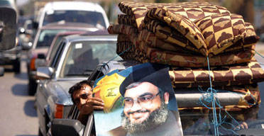 A displaced Lebanese man on his way home to south Lebanon displays a poster of the Hizbullah leader, Hassan Nasrallah. Photograph: Patrick Baz AFP /Getty Images