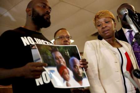 Lesley McSpadden (right), mother of 18-year-old Michael Brown, watches as Brown's father, Michael Brown Sr., holds a family picture, during a news conference, Aug. 11, 2014. 